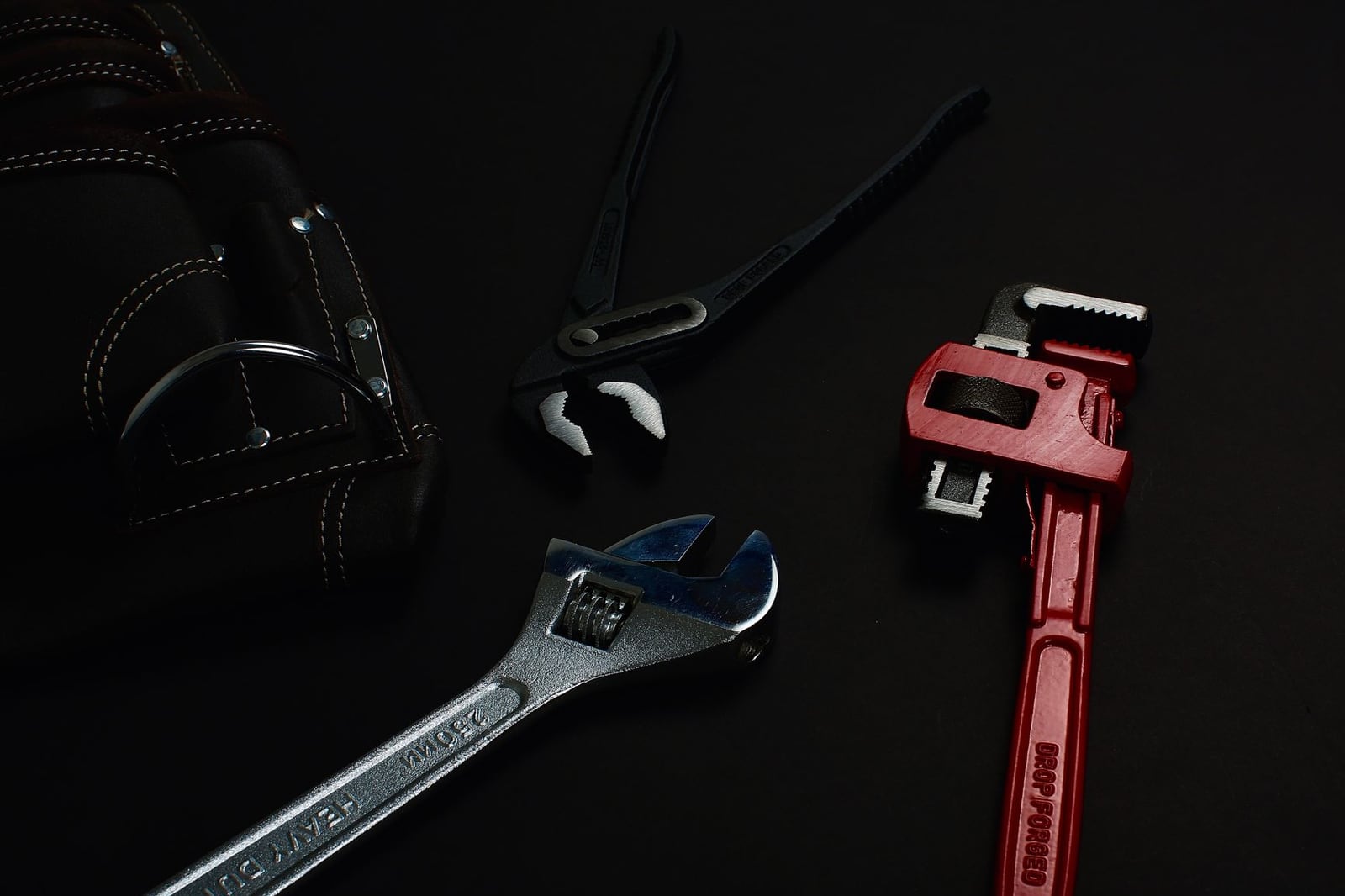 Clé serre-tube rouge et outils de plombier posés sur fond sombre