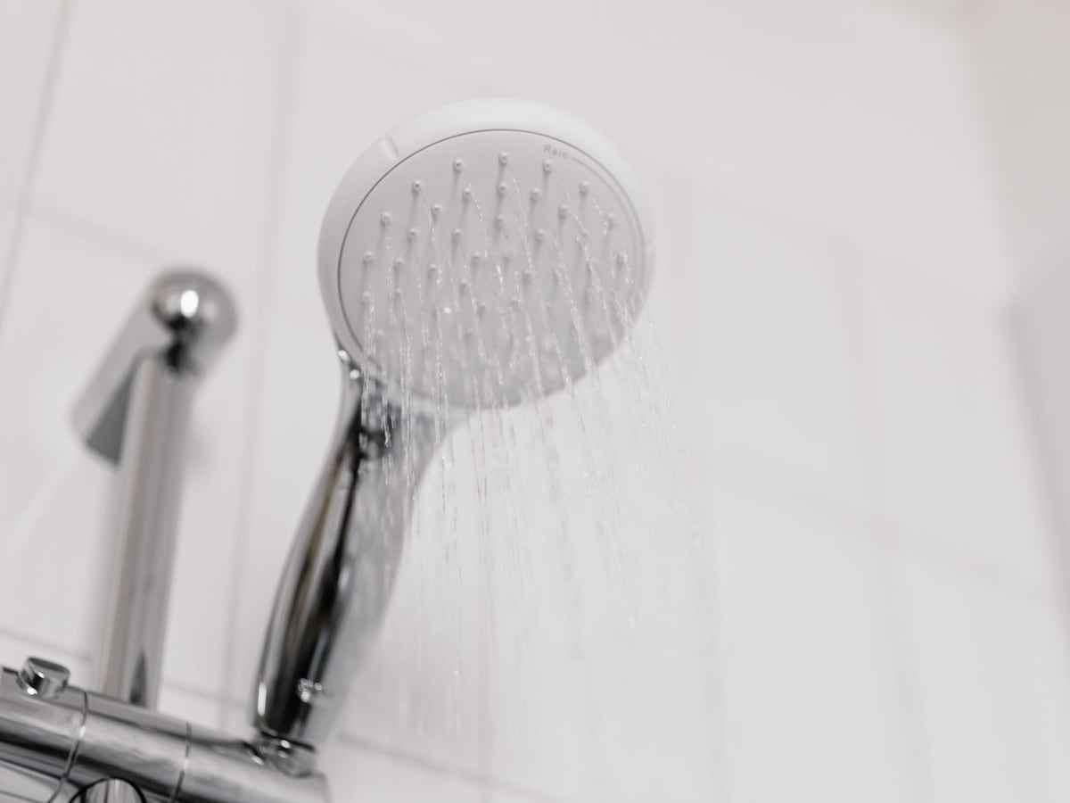 Eau chaude qui coule d'une douchette chromée en salle de bains
